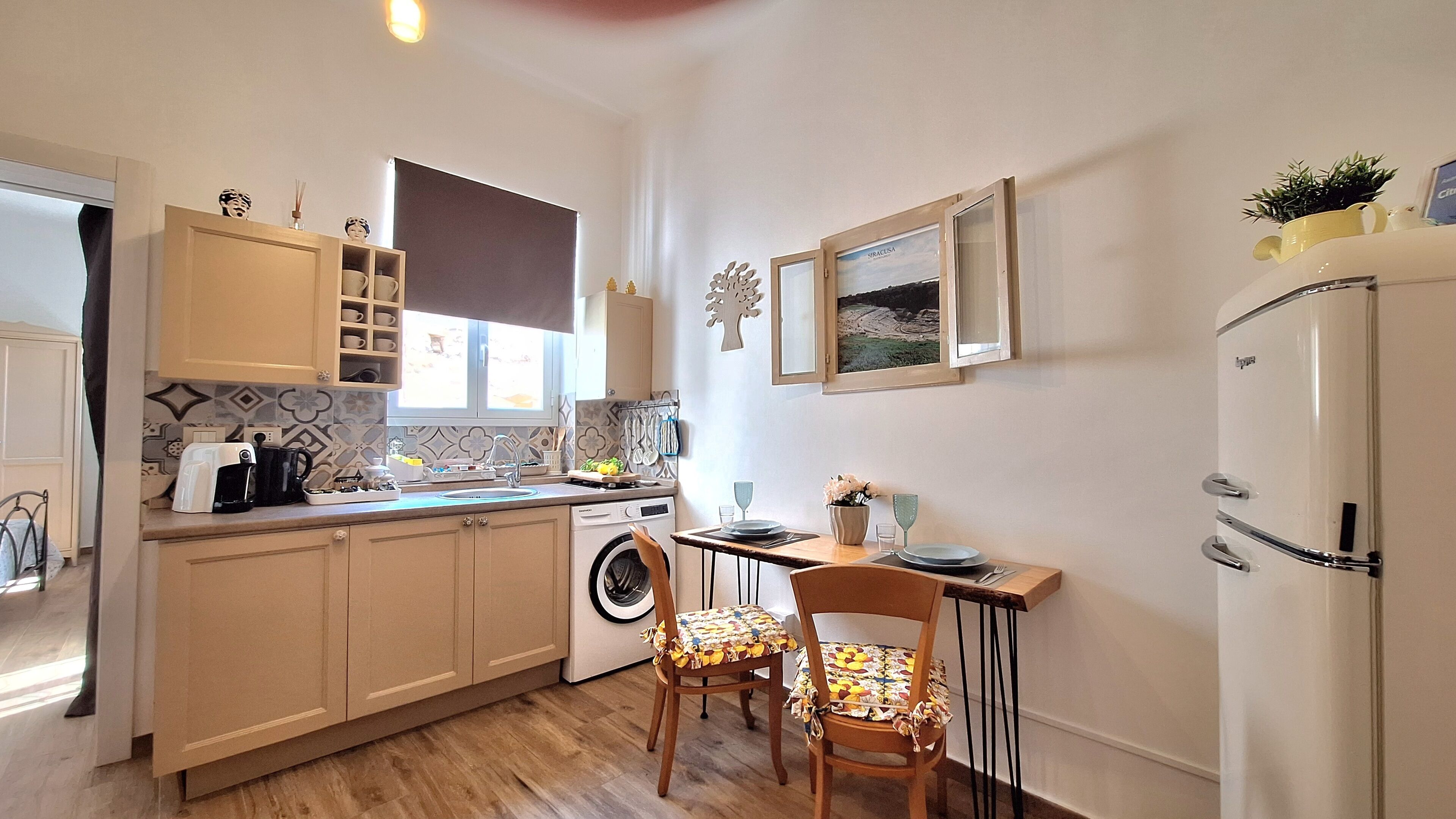 A compact kitchen with a washing machine, a dining table with chairs, and a refrigerator.