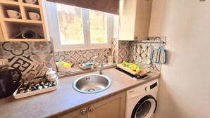 Una cocina con un lavamanos, una lavadora y una ventana con vista a un muro de piedra.