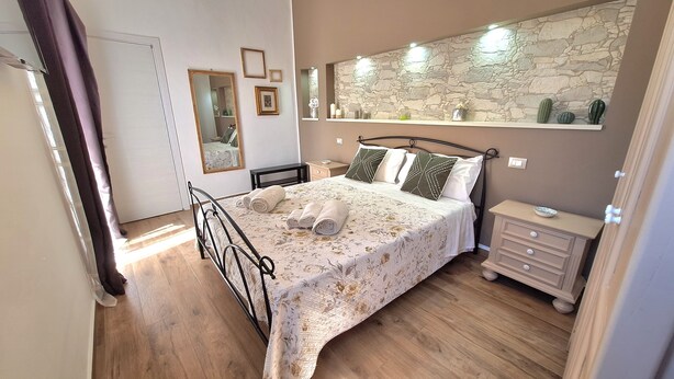 Un dormitorio con cama, mesitas de noche, un espejo y una pared de piedra.