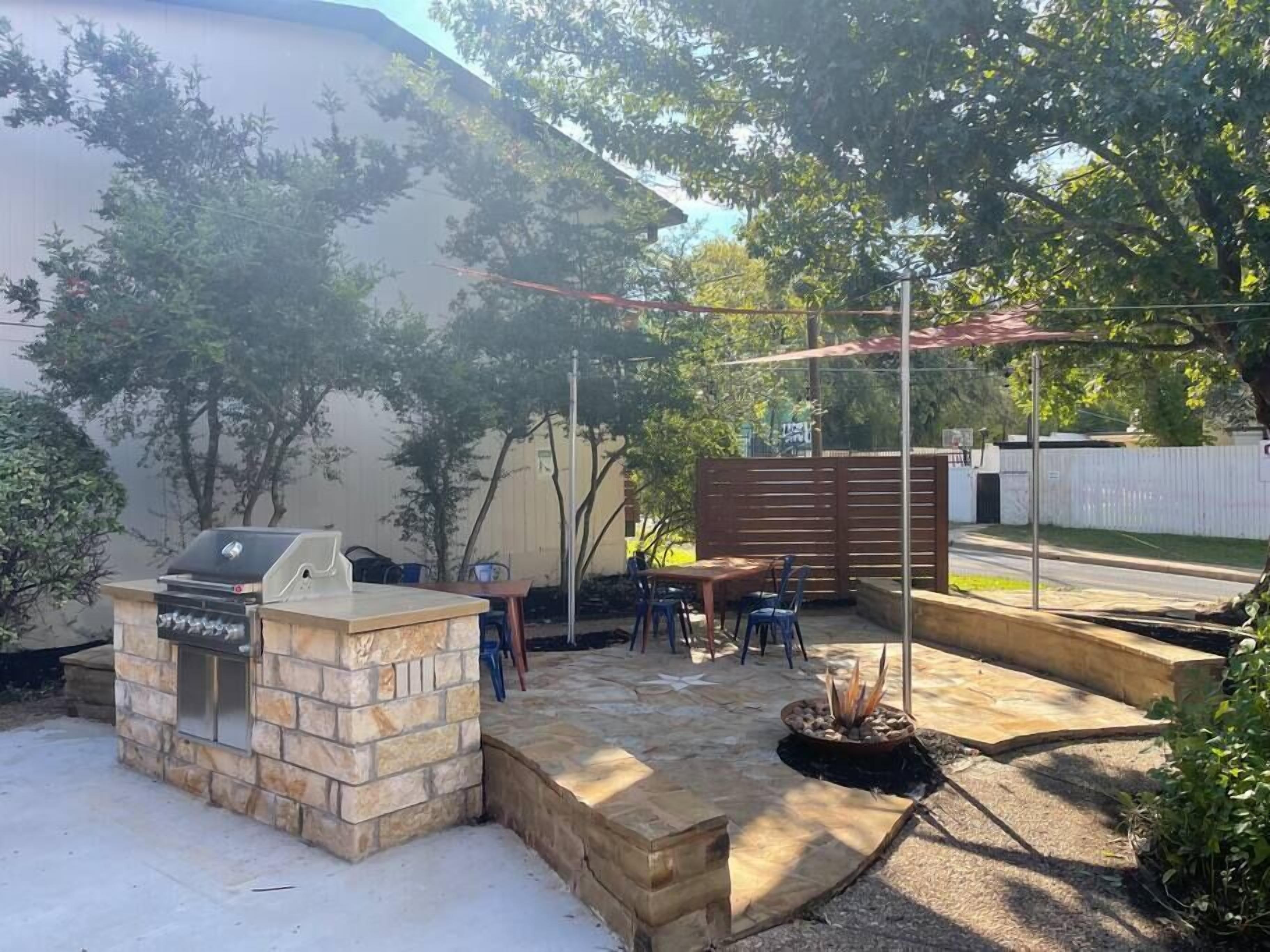 A backyard with a stone barbecue, a wooden table and chairs, and a fire pit.