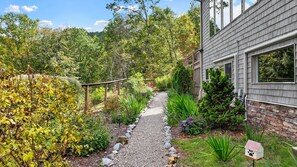 A garden pathway leading to a house with a stone foundation and a wooden deck.