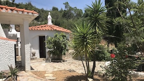 Um pátio com piso de pedra, vasos de plantas e um edifício branco com telhado ladrilhado.