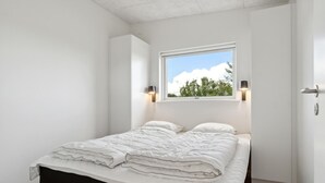 Ein Schlafzimmer mit einem Bett, zwei Nachttischlampen, einem Fenster mit Blick auf Bäume und einer Tür mit Griff.