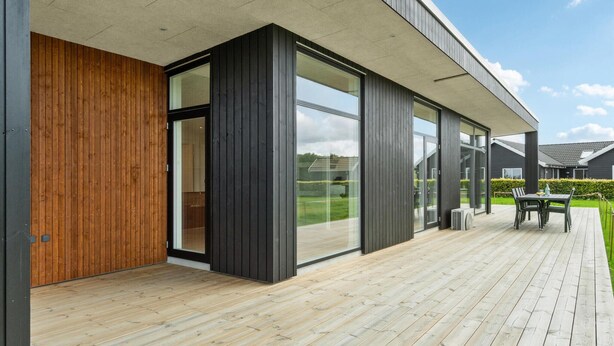 Ein modernes Haus mit einer Holzdachterrasse, großen Glasfenstern und einer Betonbrüstung.