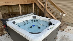 Ett bubbelbad med en kontrollpanel, omgivet av ett trädäck och en mur av tegelsten.