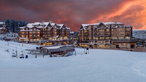 Een groot, meerhoog hotel met een skilift op de voorgrond, gelegen tegen een besneeuwd landschap en een dramatische lucht.