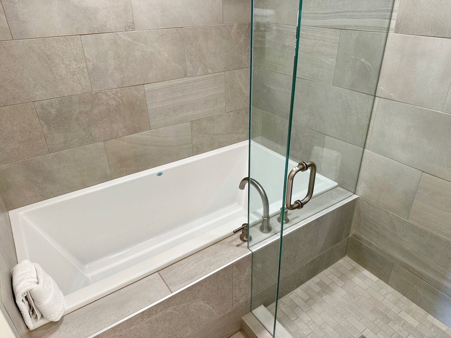 A modern bathroom with a glass-enclosed shower, a white bathtub, and beige tiles.