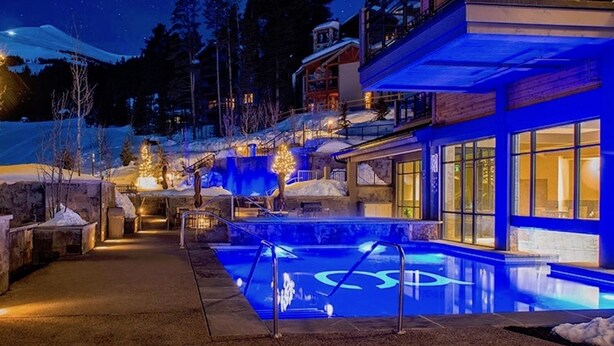 Een modern hotel met een zwembad, terras en uitzicht op het besneeuwde landschap 's nachts.