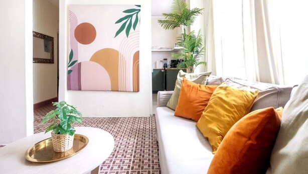Un salon comprenant un canapé, des coussins, une table basse, une œuvre d’art murale et une plante en pot.