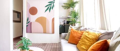 A living room with a sofa, cushions, a coffee table, a wall art piece, and a potted plant.