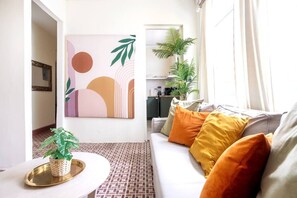 A living room with a sofa, cushions, a coffee table, a wall art piece, and a potted plant.