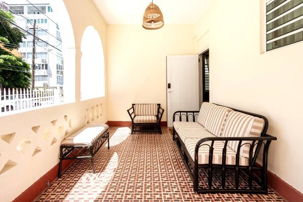 A balcony with a patterned floor, a sofa, a chair, and a hanging light fixture.