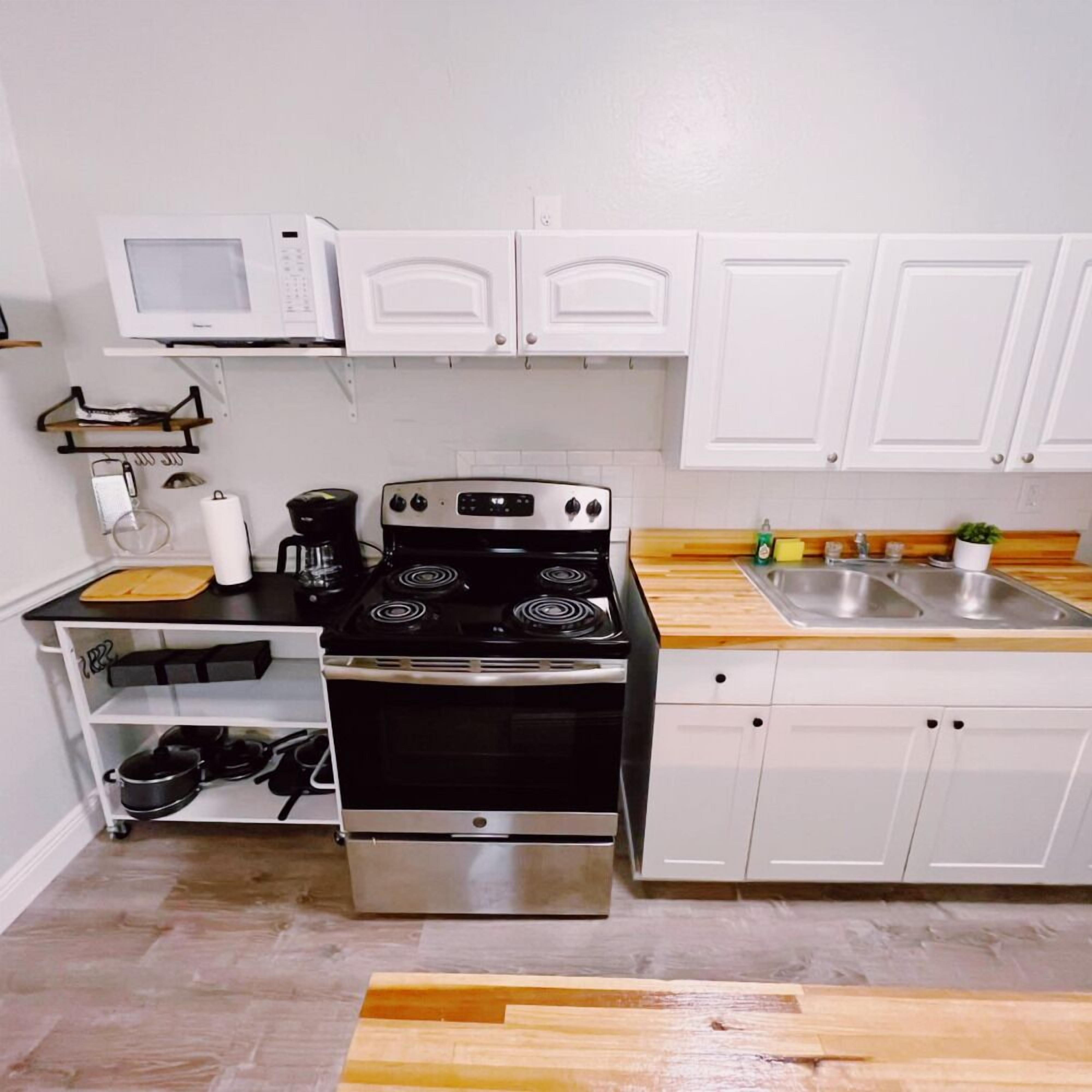 Una cucina compatta con mobili bianchi, un fornello, un forno a microonde e un lavandino.