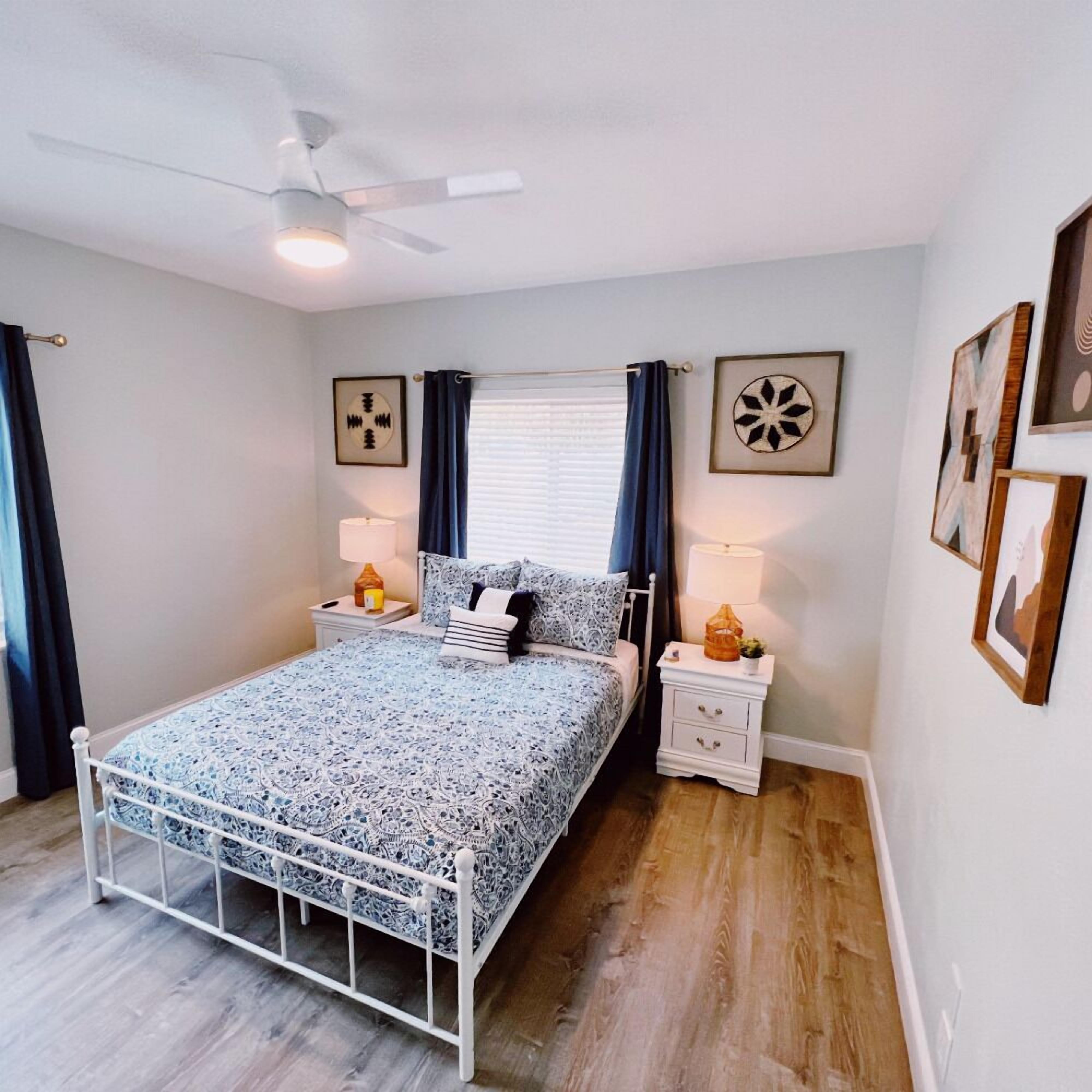 A bedroom with a bed, nightstands, a ceiling fan, and wall art.