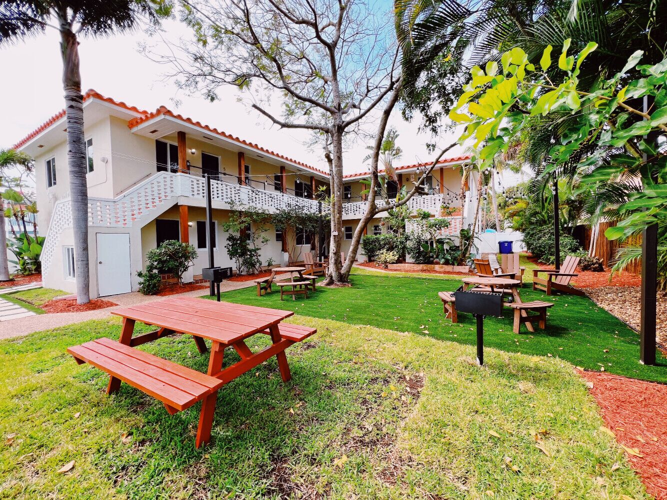 A building with a balcony and a garden area with picnic tables and chairs.