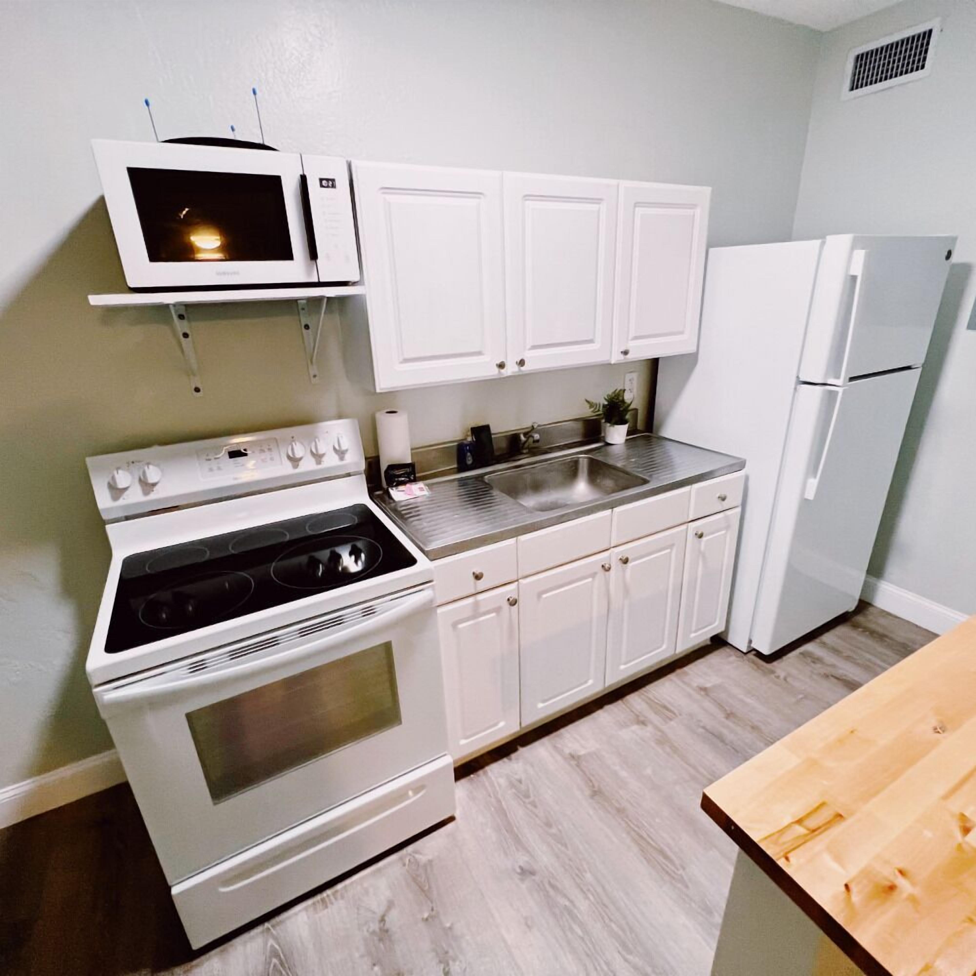 A compact kitchen with white cabinets, a stove, a microwave, and a refrigerator.