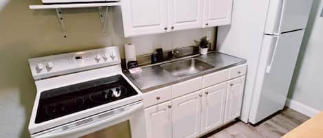 A compact kitchen with white cabinets, a stove, a microwave, and a refrigerator.
