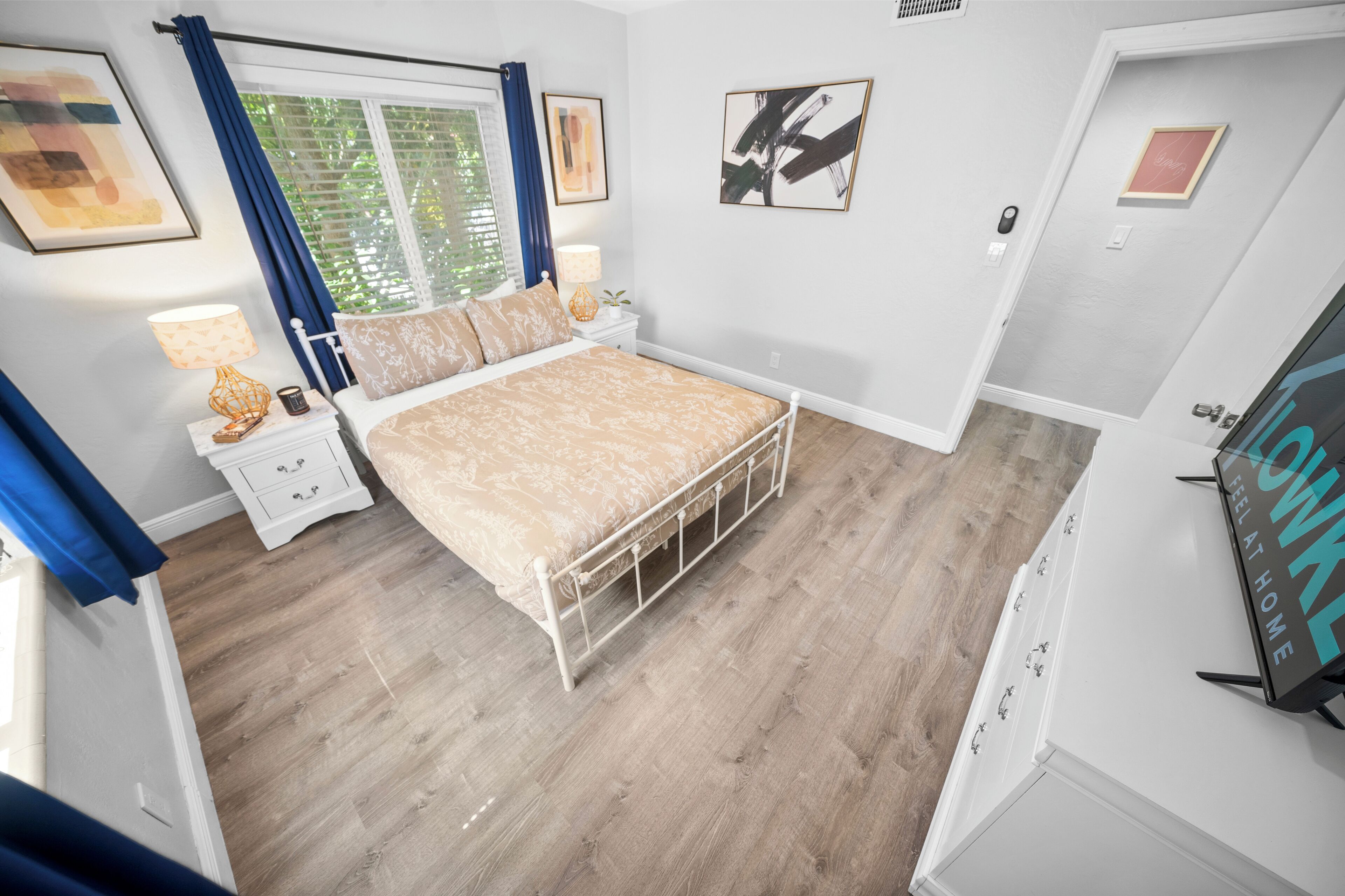 A bedroom with a bed, nightstands, a window with curtains, and wall art.