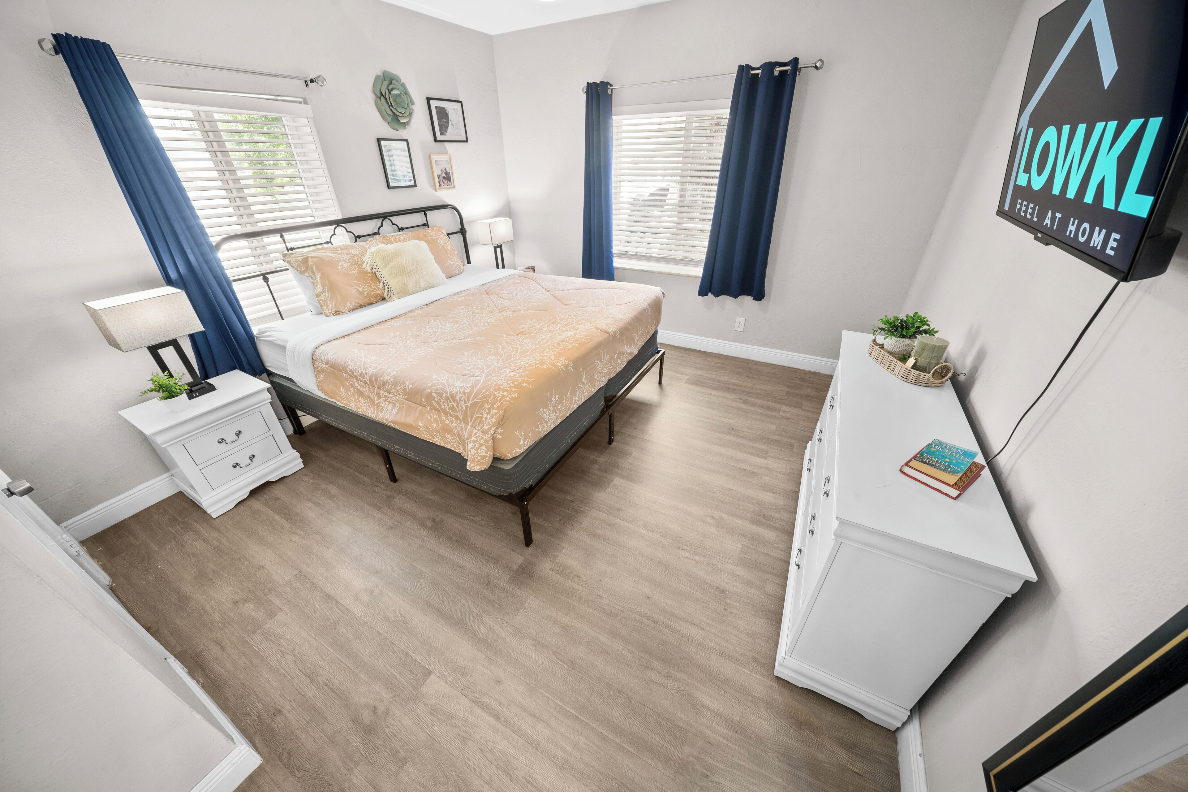 A bedroom with a bed, bedside tables, a dresser, a TV, and a window with curtains.