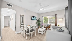 Una sala moderna con comedor, ventilador de techo, televisor y ventana con persianas.