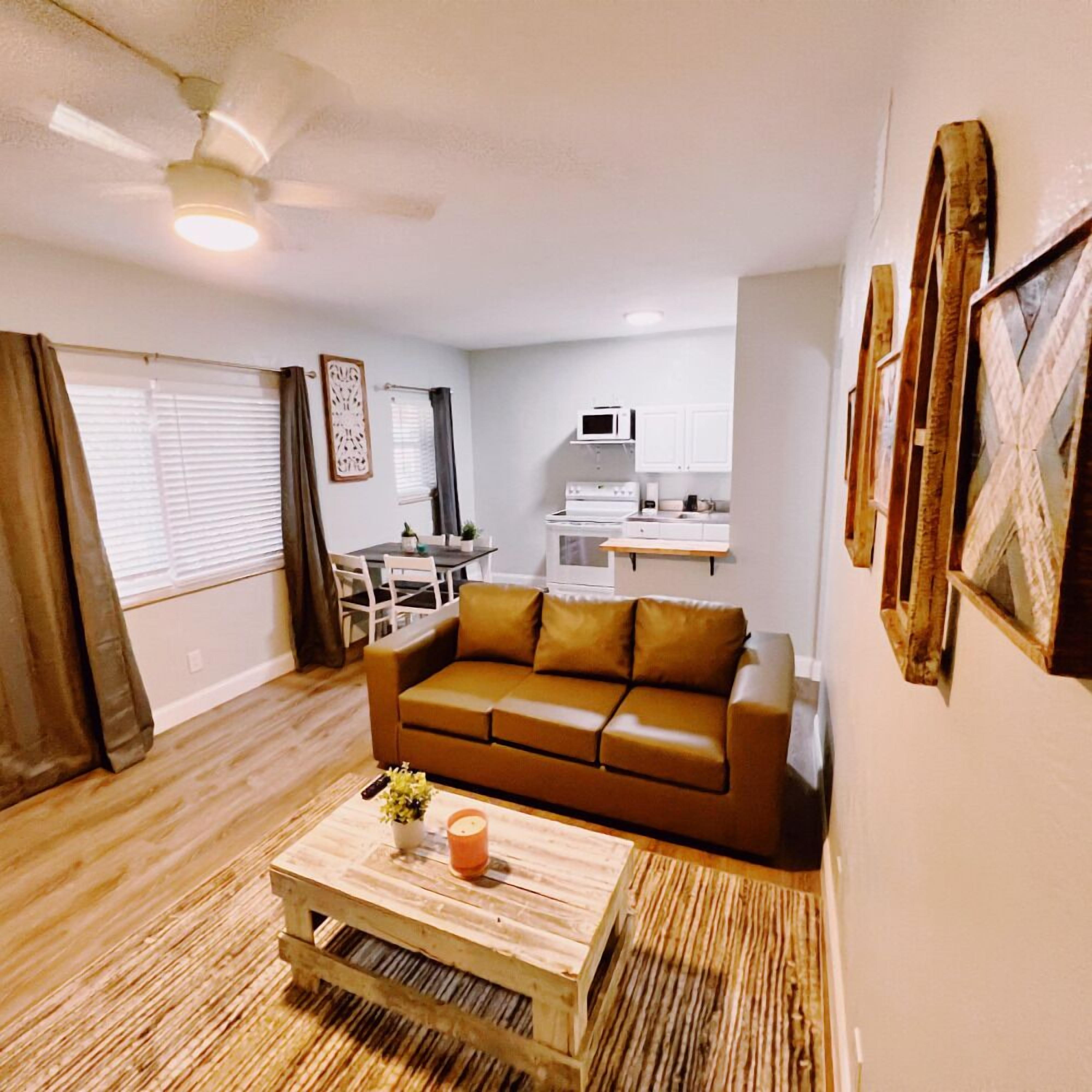 A living room with a brown sofa, a wooden coffee table, and a dining area with a table and chairs.