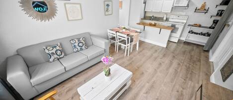 A modern living room with a grey sofa, a coffee table with a vase, and a dining area with a table set for four.