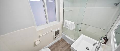A bathroom with a shower, toilet, sink, and a window.