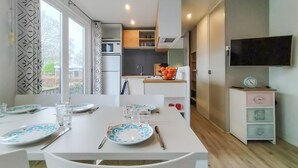 A compact kitchen with a microwave, oven, and sink. There is a dining table with plates and cutlery, and a TV mounted on the wall. - 3 bedroom amazing home in Heinkenszand (Heinkenszand)