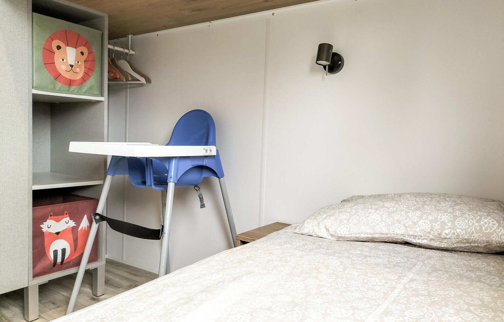 Une chambre à coucher avec un lit, une chaise haute bleue, une armoire décorée d’un motif représentant un lion et un renard, et un luminaire fixé au mur.