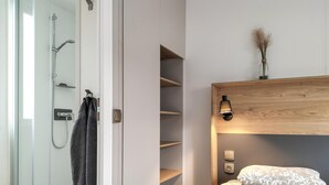 A modern bathroom with a glass shower enclosure, a towel rack, and a wooden shelf unit with a wall-mounted light. - 3 bedroom amazing home in Heinkenszand (Heinkenszand)