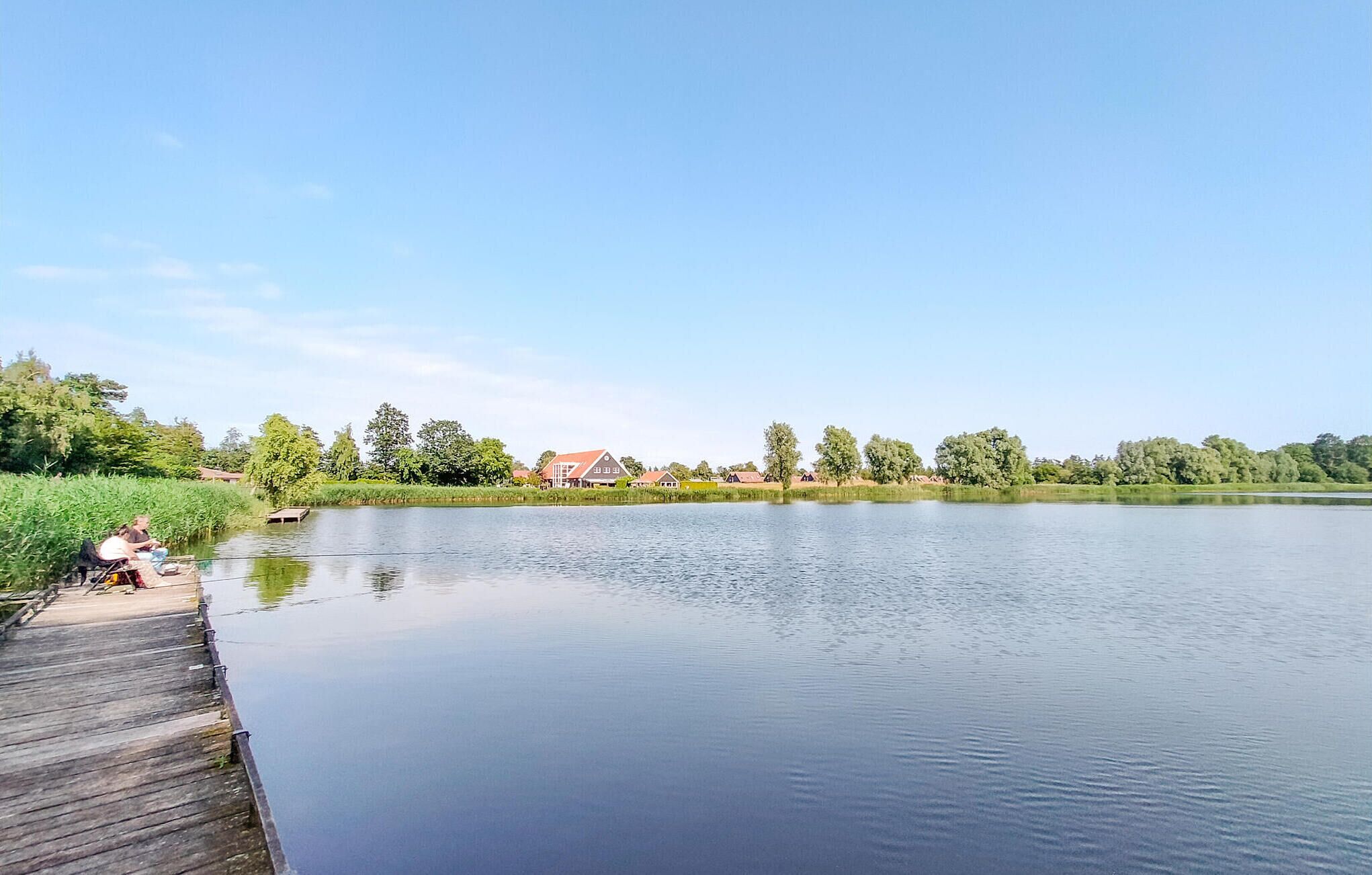 A calm lake with a wooden dock and houses in the background.