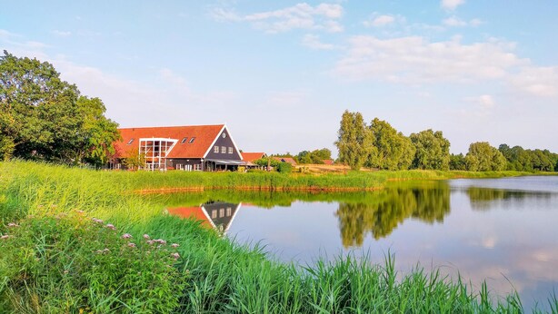 A traditional Dutch house with a red roof, situated beside a calm lake with lush greenery and trees in the background. - 3 bedroom amazing home in Heinkenszand (Heinkenszand)