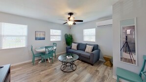 Un salon moderne avec un canapé gris, des fauteuils turquoise, une table basse en verre et un ventilateur de plafond.