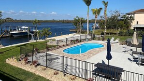 Une piscine avec vue sur l’eau, entourée de palmiers et donnant sur un quai où sont amarrés des bateaux.
