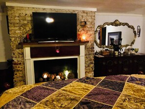 A room with a brick fireplace, a television mounted above it, a mirror with an ornate frame, and a bed with a quilt. - 18th Cent. Charm in Historic Downtown Annapolis (Annapolis)
