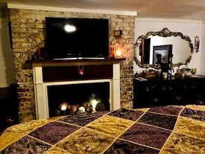 Cozy room with a fireplace, television, and a comfortable bed, featuring a patterned quilt and ornate mirror.