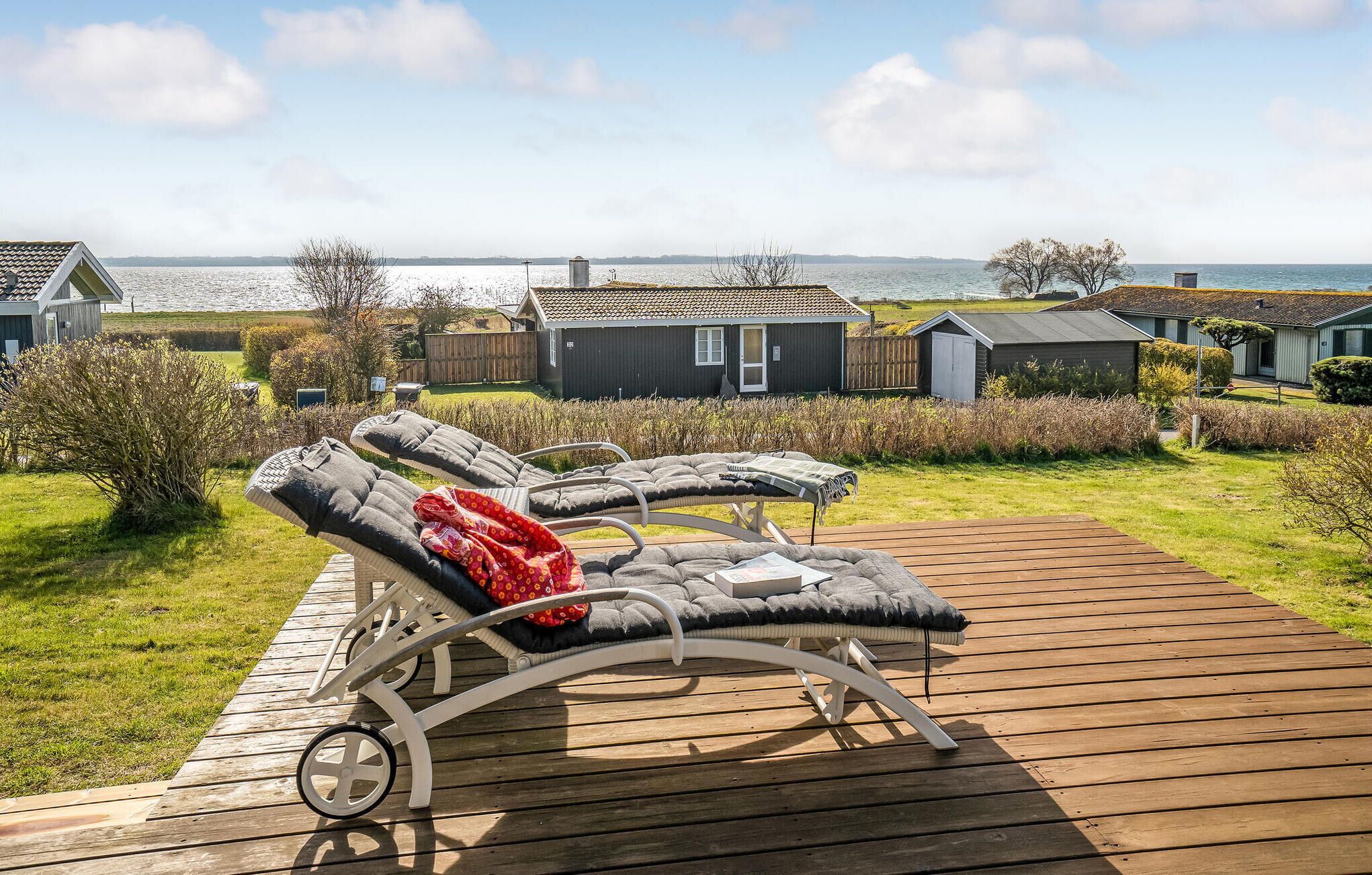 Ett däck med solstolar och en trägång som leder till ett hus med utsikt över havet.