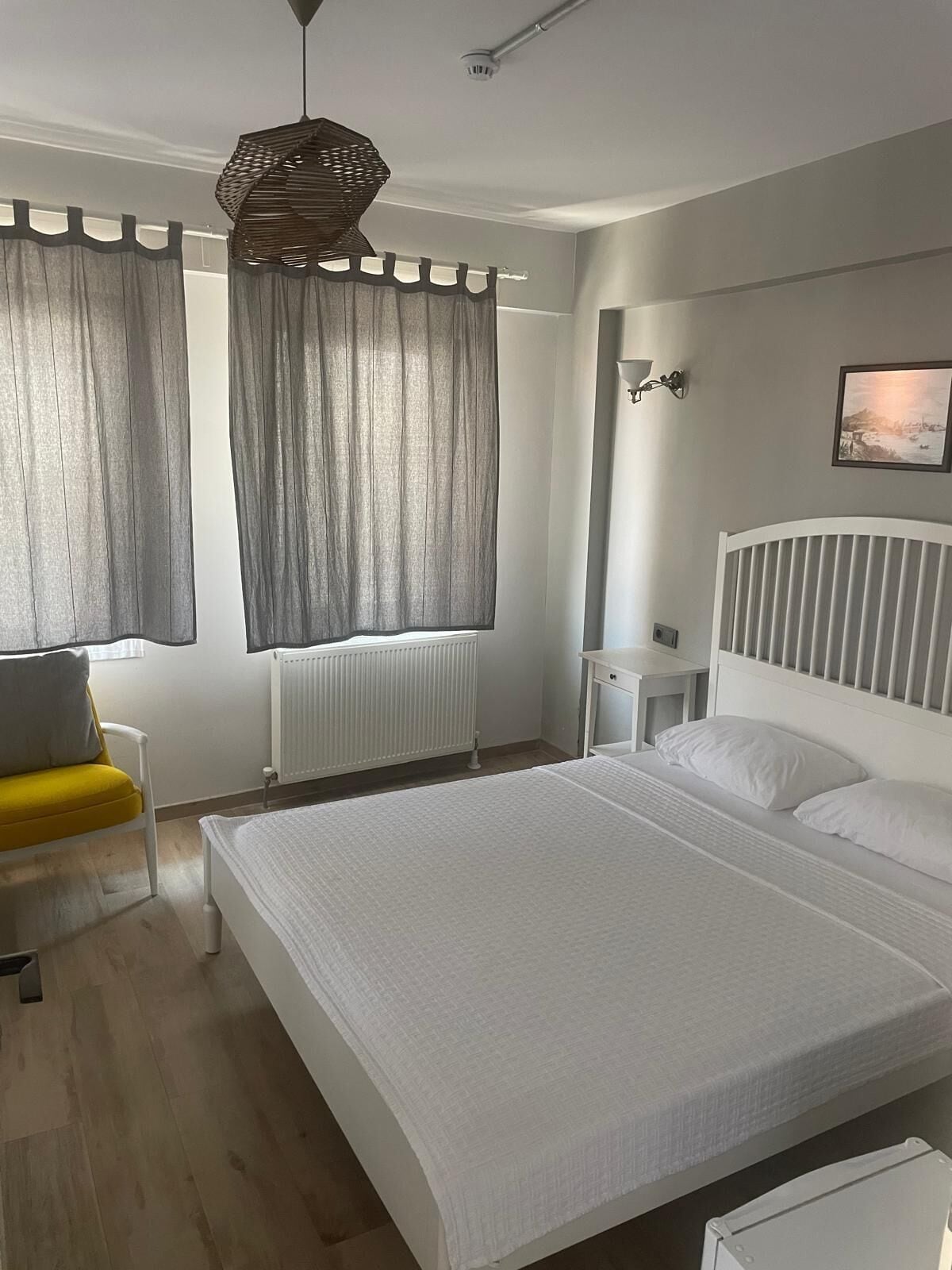 Un dormitorio con cama, una silla, una mesita de noche, una lámpara y una ventana con cortinas.