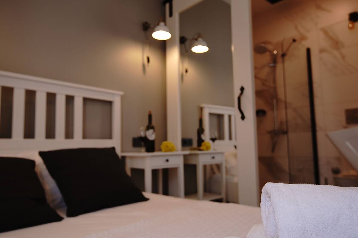 Quarto com cama, mesa de cabeceira, espelho e chuveiro.
