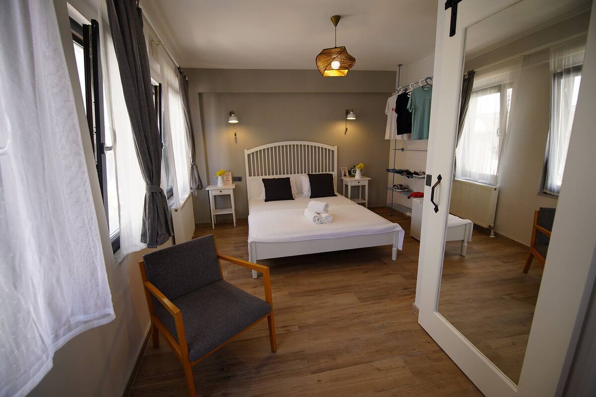 Quarto com cama, mesas de cabeceira, uma cadeira e luminária pendente.