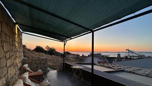 Una terraza en la azotea con sillones, una mesa y vistas al atardecer sobre el mar.