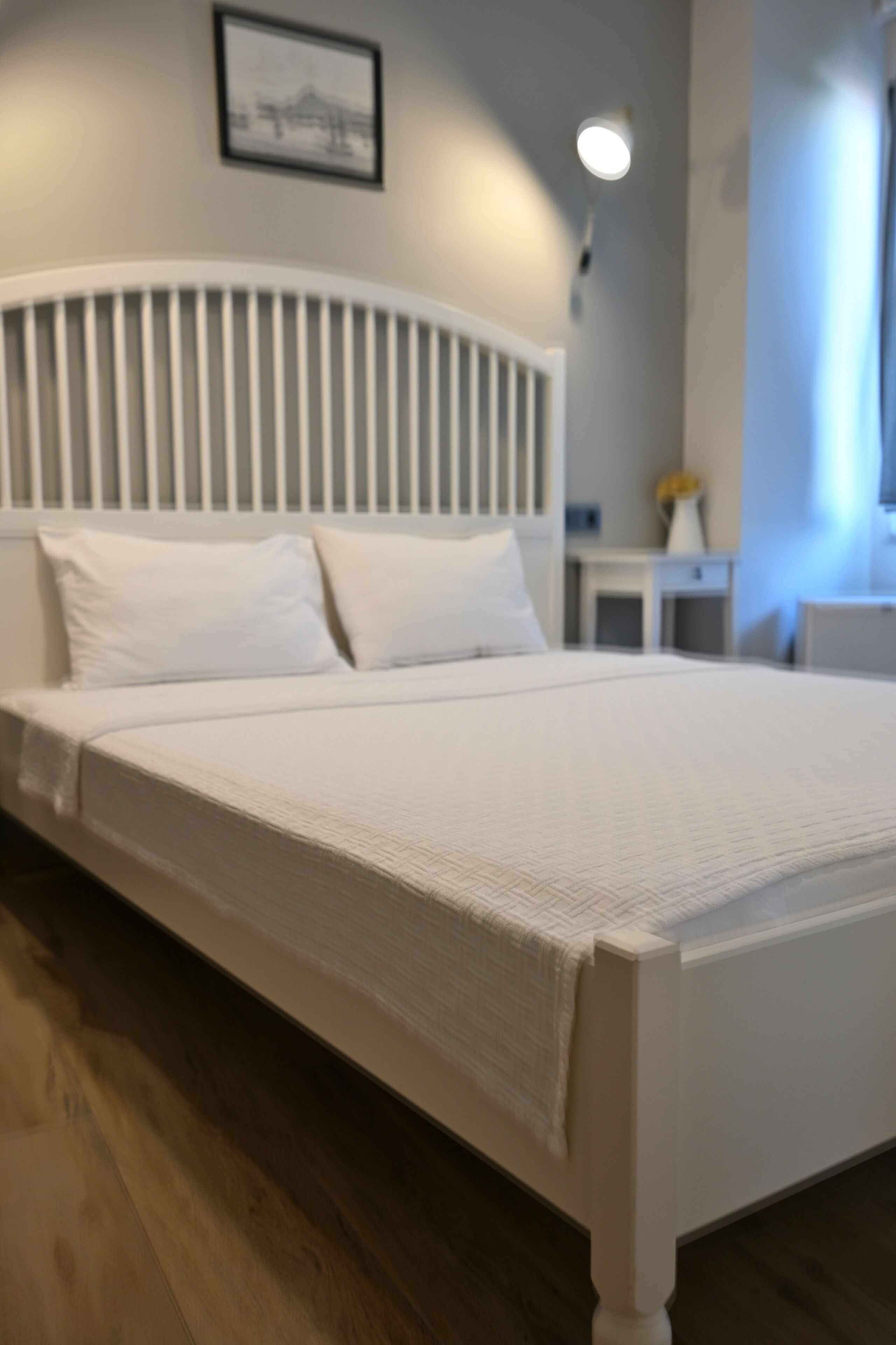 Una cama blanca con cabecera, una mesita de noche y un cuadro en la pared.