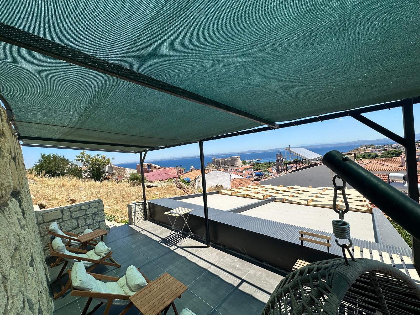 A terrace with outdoor seating, a view of the sea, and a historic building in the background.