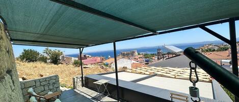 A terrace with outdoor seating, a view of the sea, and a historic building in the background.