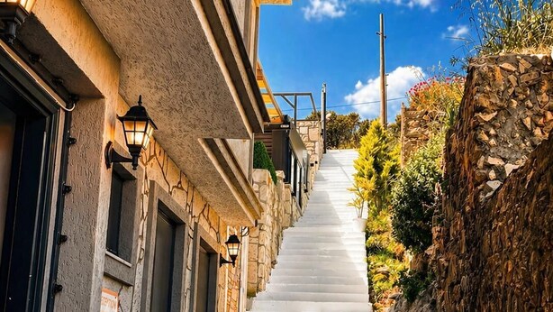 Una escalera que sube hacia un edificio con paredes de piedra y barandilla metálica.