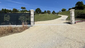 Un camino de grava que conduce a una entrada portonada con un pilar de piedra y una valla decorativa.