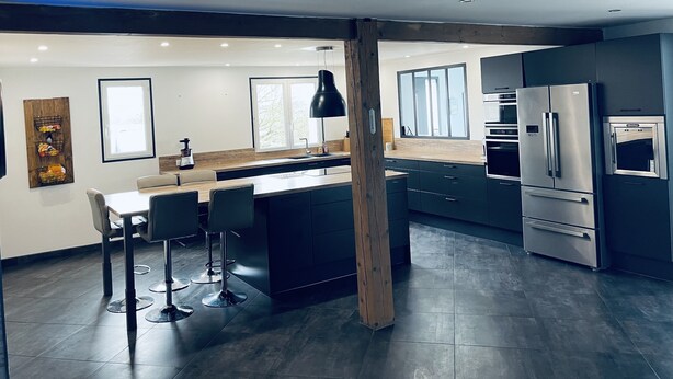 Una cocina moderna con muebles oscuros, electrodomésticos de acero inoxidable y una isla central con taburetes de bar.