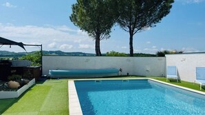 Una piscina rectangular con agua cristalina azul, rodeada por un muro blanco y una zona cubierta de césped.