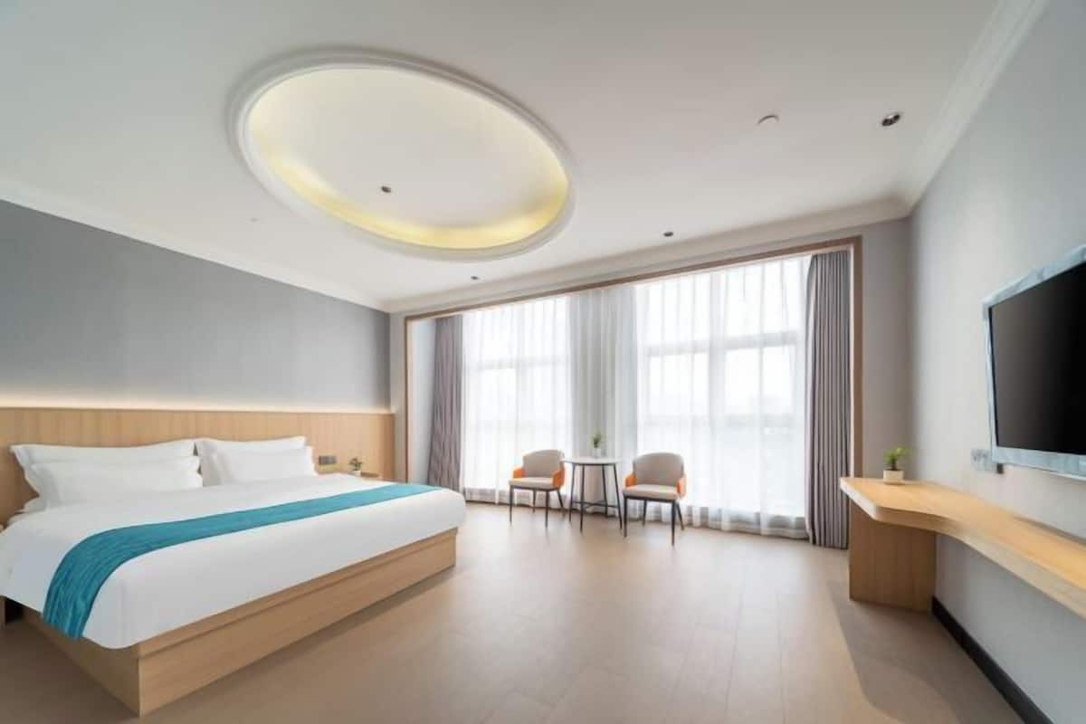 A hotel room with a bed, a TV, a desk, and a window with curtains.