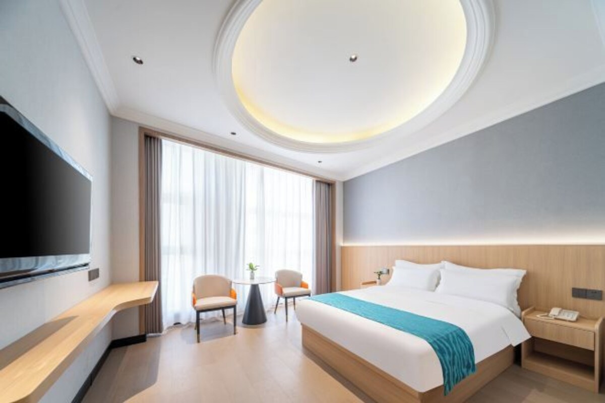 A modern hotel room with a large bed, a flat-screen TV, a desk, and a chair.